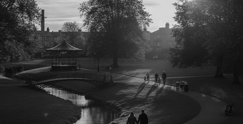 Early morning walkers on a winding path in Tameside park, illuminated by a streetlamp at sunrise with rolling hills in the distance.